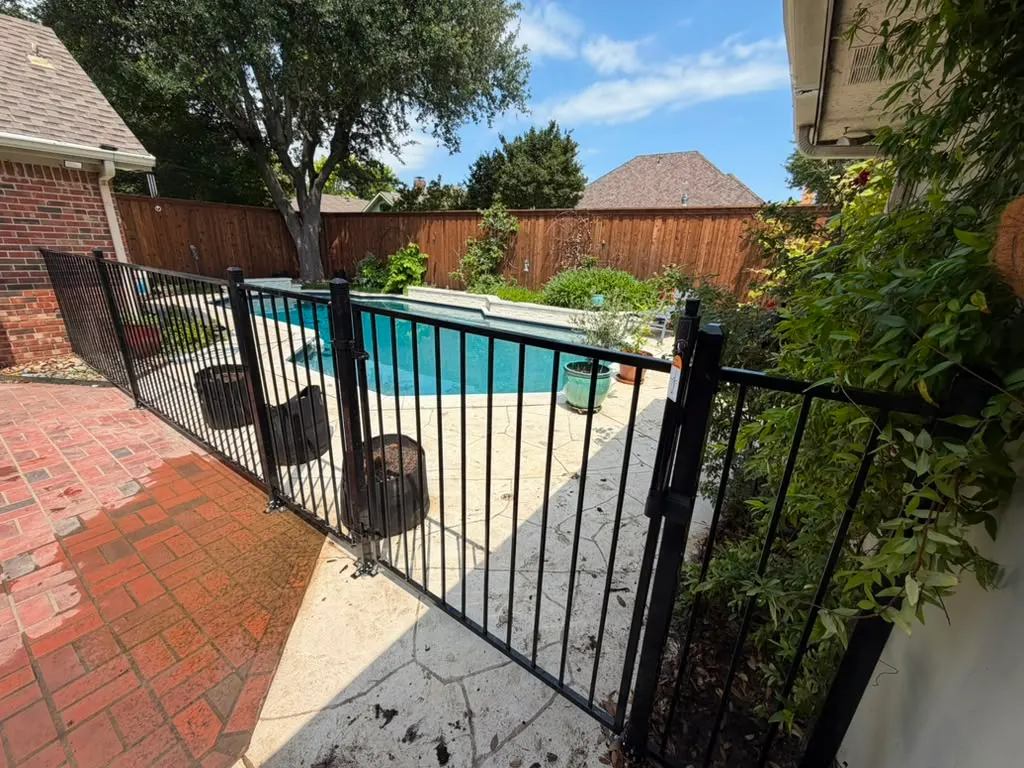 Black metal safety fence and gate installed around a backyard pool