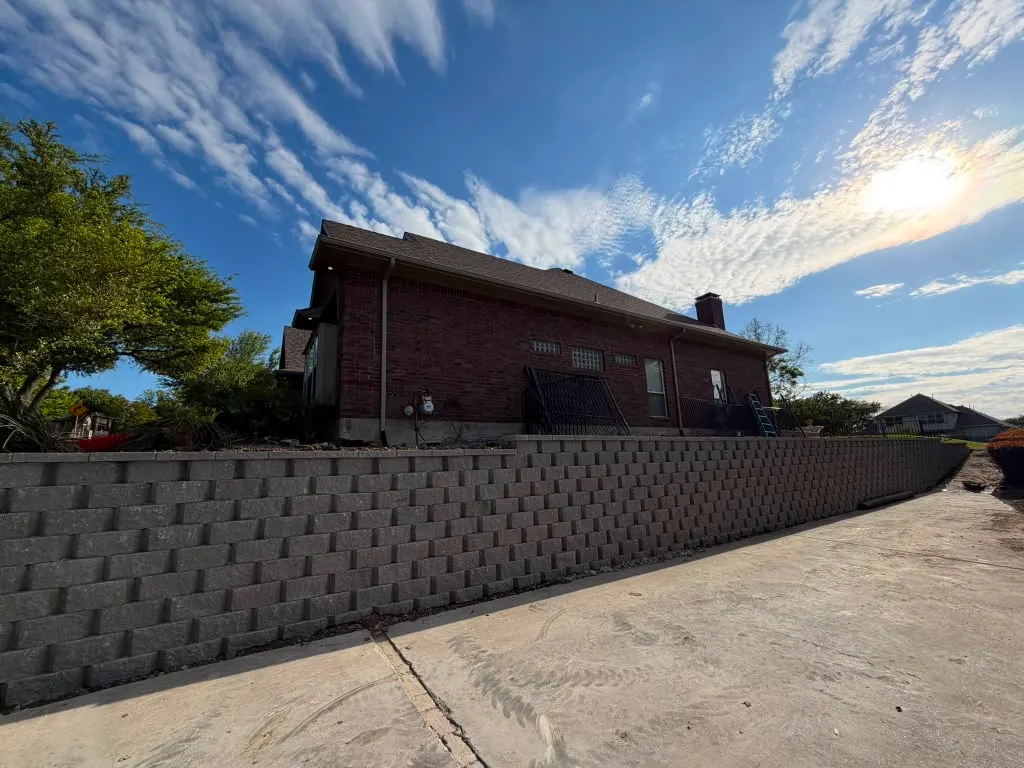 Long concrete block retaining wall beside a brick home
