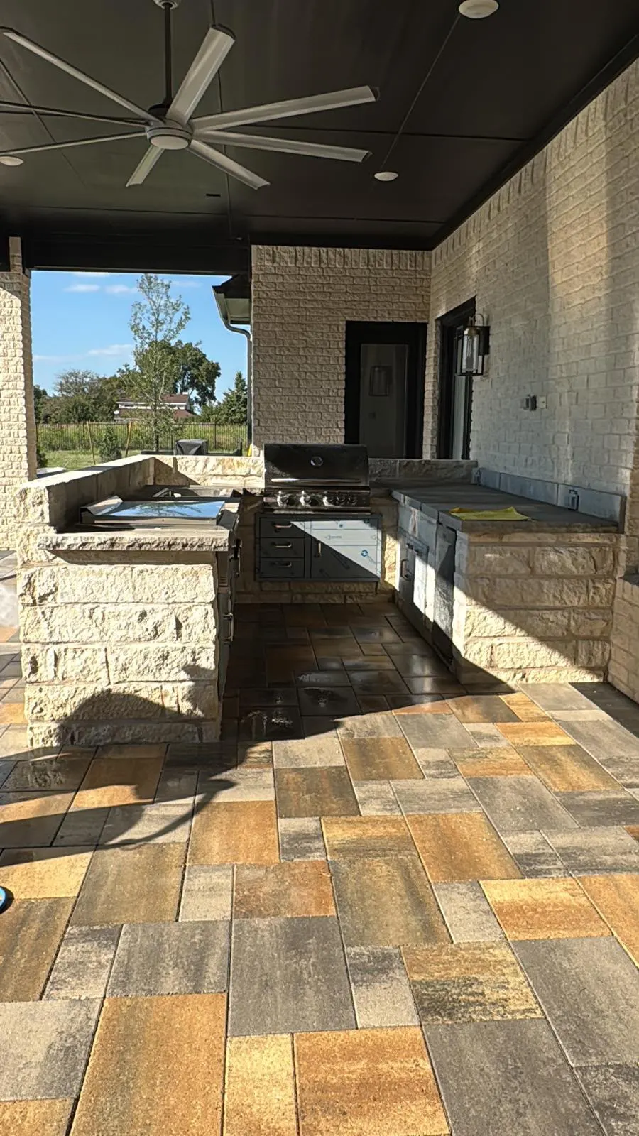 Covered outdoor kitchen with grill, stone counters, pavers, and ceiling fan