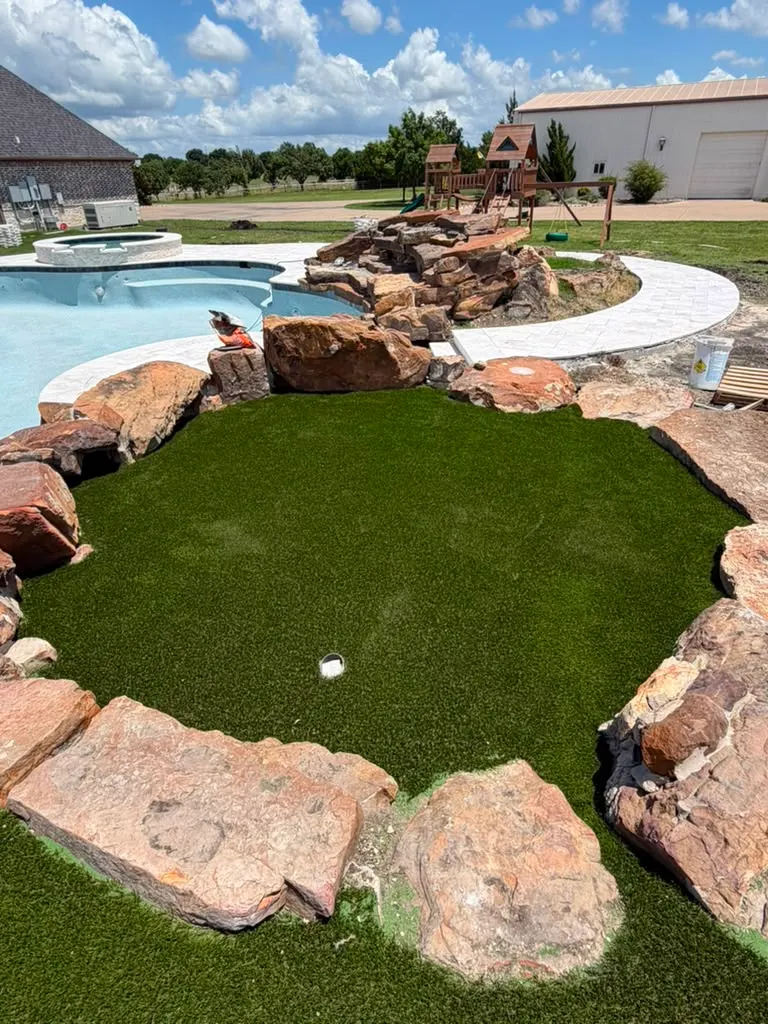 Artificial turf landscape framed by natural stone beside a pool