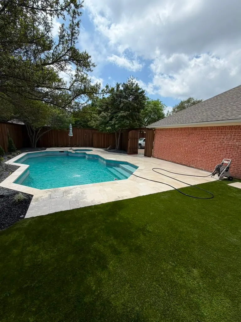 Completed backyard pool area with artificial turf and light stone decking