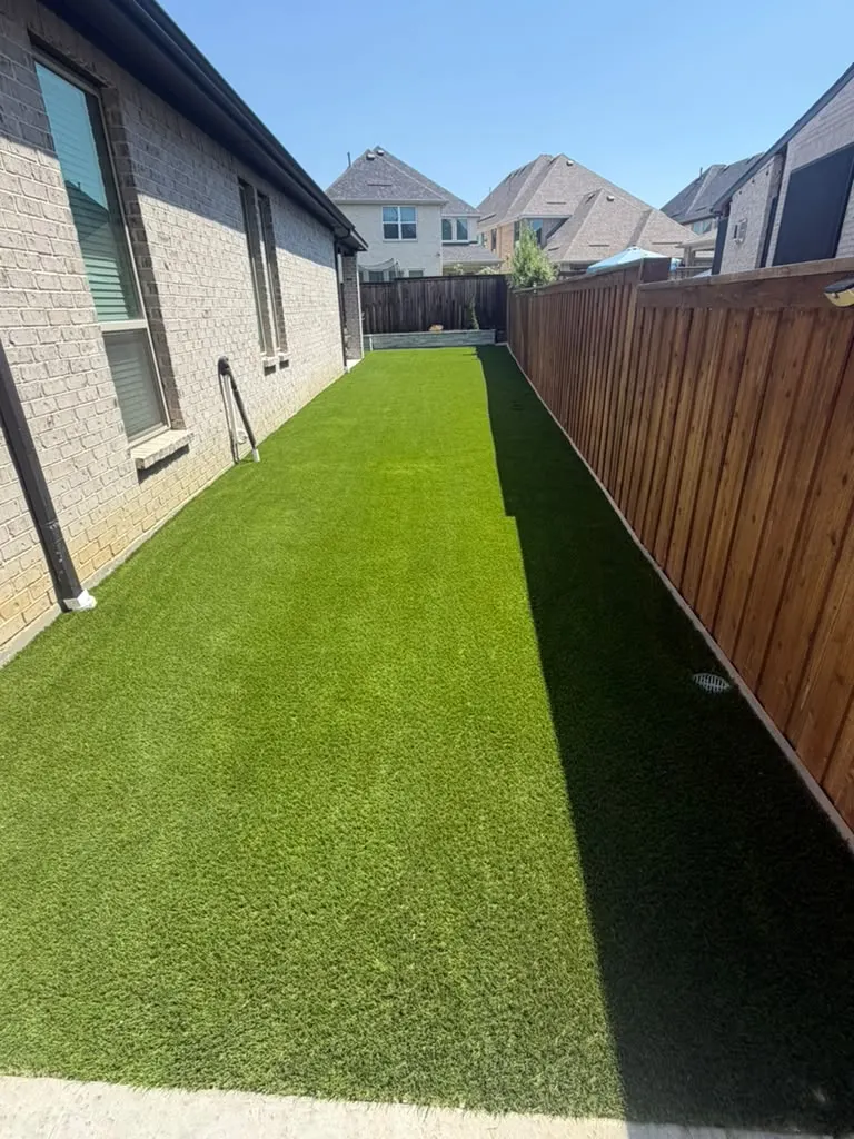Long artificial turf installation between a brick home and wood privacy fence